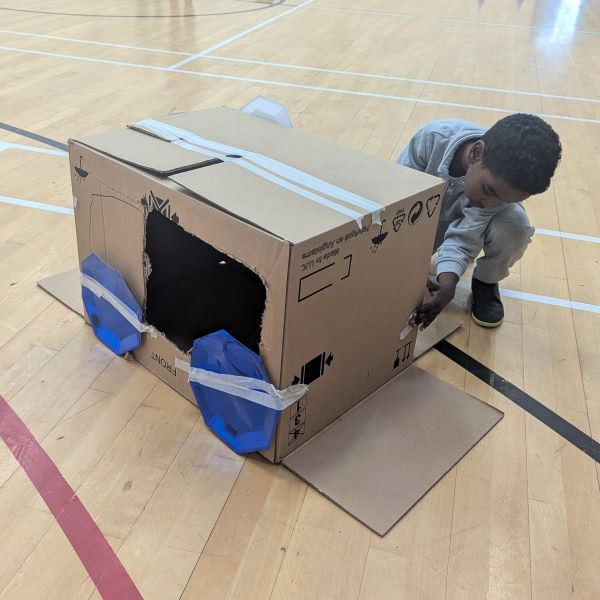 Bachgen yn chwarae gyda char cardbord